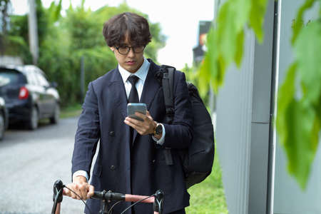 Young asian businessman looking at messages on mobile phone while riding bicycle in the city.の写真素材