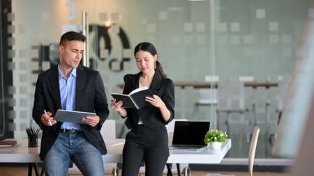 Successful businessman and elegant female manager standing in modern office and having a business talkの写真素材