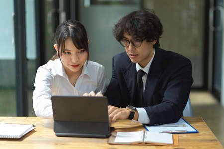 Young businessman and businesswoman collaborate on a digital tablet. A male IT assistant is troubleshooting IT issues on a female tablet.の写真素材