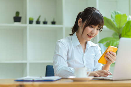 Pretty millennial female assistant using smart mobile phone during her work hour in the office.の写真素材