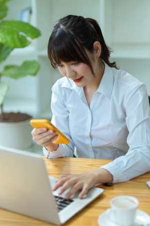 Charming young woman business worker looking the informations on smartphone while working on laptop.の写真素材