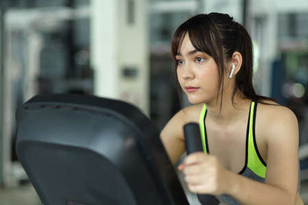 Close-up of sporty asian woman cycling on a fitness bike machine at the gym. exercise and sport.の写真素材