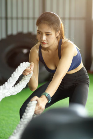 Elegant asian female in sport club exercising on battle ropes program for muscular bodybuilding.の写真素材