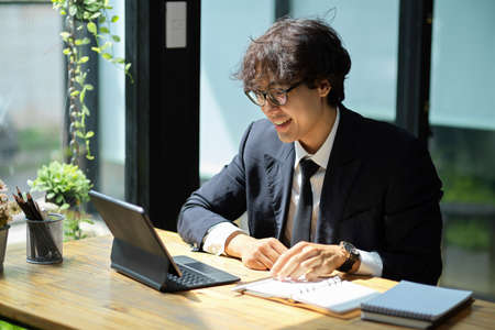 Asian businessman sits near by the window glass and manage his work on digital tablet computer.の写真素材