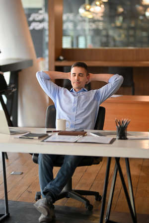 Happy successful caucasian businessman chilling and resting at his working desk in modern office.の写真素材