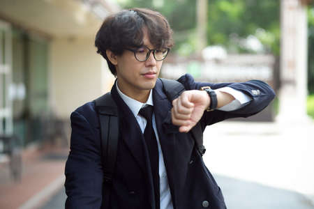 Handsome young businessman checks the time on his wristwatch while walking down the street.の写真素材