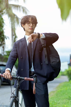 Portrait of Urban businessman in business suit looking on his wristwatch while going to work by bikeの写真素材