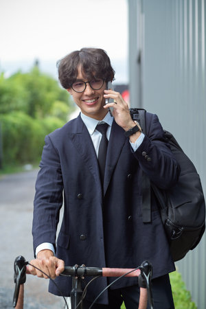 Portrait of asian businessman in business suit talking on the phone while going to work by bike.の写真素材