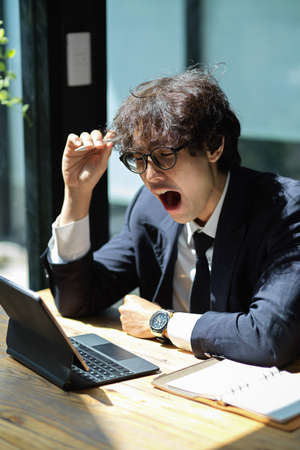 Tired salaryman works on his digital tablet computer and feels sleepy at his workstation. overworkedの写真素材