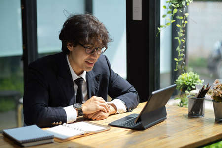 Businessman in business suit and eyeglasses doing online conference meeting via tablet at his desk.の写真素材