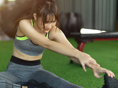 Attractive young fit woman cool down after workout, exercise stretching her leg at the fitness gym.の写真素材