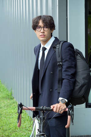 Millennial male officer worker in formal suit standing with his bicycle in front of the building.の写真素材