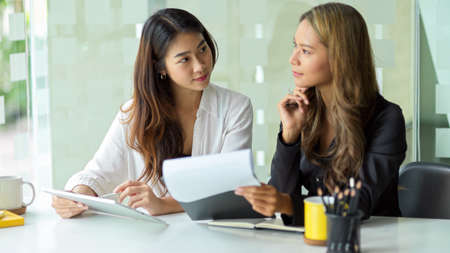 Two attractive businesswomen are meeting and evaluating business marketing solutions in the office.の写真素材