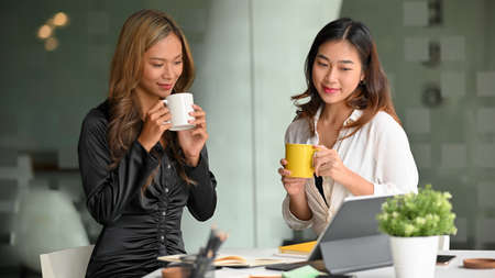 Cheerful businesswomen sip coffee while holding a small meeting to discuss the next steps for a new campaign in the office.の写真素材