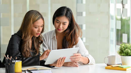 Concentrated businesswomen look at the business financial statement report together via portable tablet.の写真素材