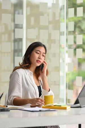 Attractive female entrepreneur on the phone with business supplier, contact with business partner.の写真素材