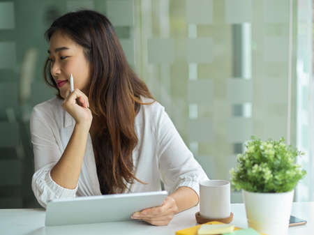 Young asian female business employee using tablet while listening her colleagues explain work process in the meeting.の写真素材