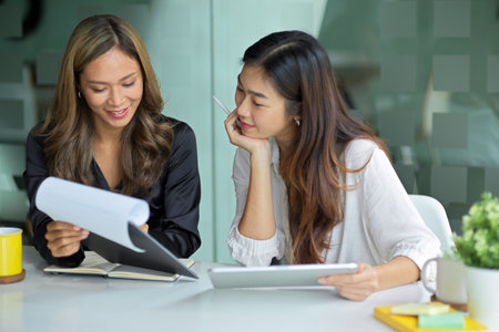 Happy businesswomen reading information on paperwork and chatting about the process in modern officeの写真素材
