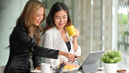 Happy businesswomen sip coffee while talking and watching funny video in their lunch break together.の写真素材