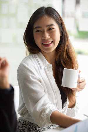 Portrait of beautiful asian young businesswoman having a nice conversation while taking a coffee break. holding coffee cup.の写真素材