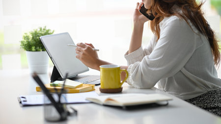 Close-up image of confident business female entrepreneur talking on the phone with business partners and taking notes on digital tablet.の写真素材