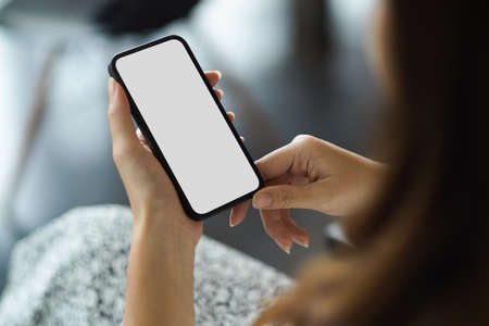 Female holding modern smartphone with white screen mockup and blurred background. wireless device...
