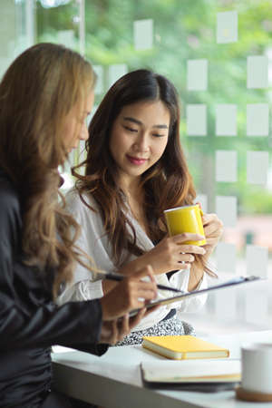 A beautiful and friendly female manager assist her assistant review her project's paperwork in office.の写真素材