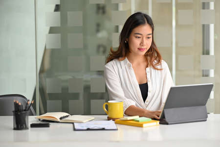 Motivated asian young businesswoman planing her strategy while typing on laptop in her office.の写真素材