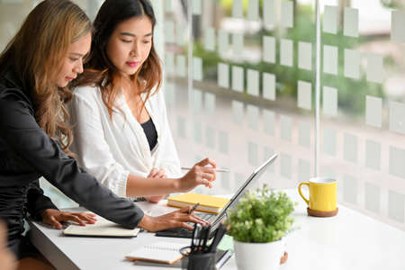 Two asian businesswoman having an informal meeting, listening to her colleague with a pensive expression in co working area.の写真素材