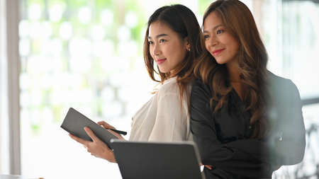 Asian young businesswoman sitting back to back with crossed hands in the office. Business partner, teamwork.の写真素材