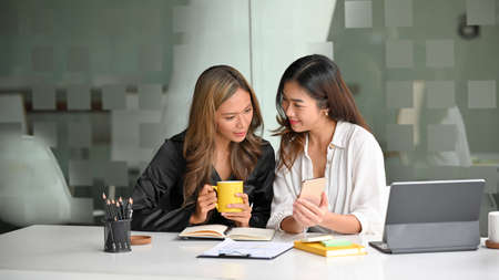 Female colleagues were having an interesting conversation while showing some content on their smartphones.の写真素材