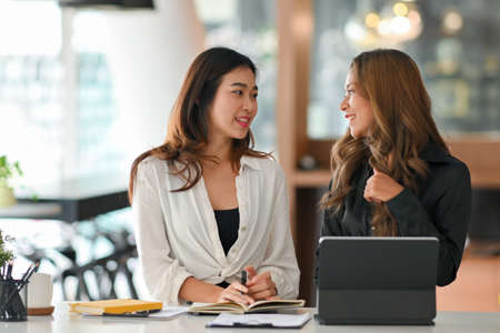 Business concept. Beautiful woman talking with her colleague while sitting at desk in office room.の写真素材