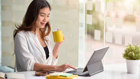 Beautiful female entrepreneur working on a business project on a tablet computer while resting and sipping hot tea.の写真素材