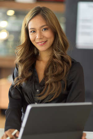 Portrait of Confident asian young businesswoman in black dress sits in front of her working desk in office.の写真素材