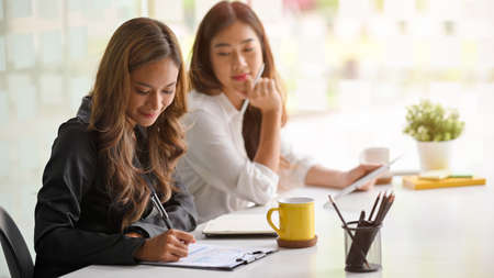 Team work process. Two asian businesswomen with financial report papers in bright office.の写真素材