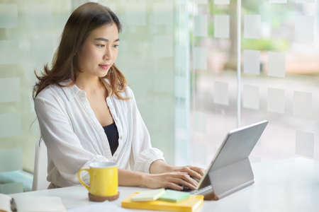 Successful asian young business woman working on digital tablet computer at her modern office room.の写真素材