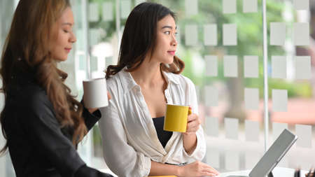 Relaxed businesswomen having a coffee together at office break room  in the morning.の写真素材