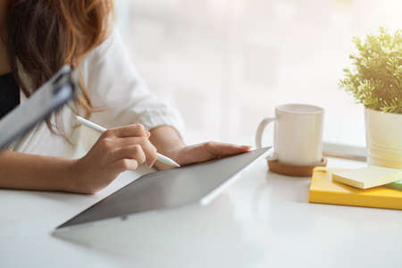 Close-up motivated businesswomen using stylus pen with digital touchpad tablet computer at her desk.の写真素材