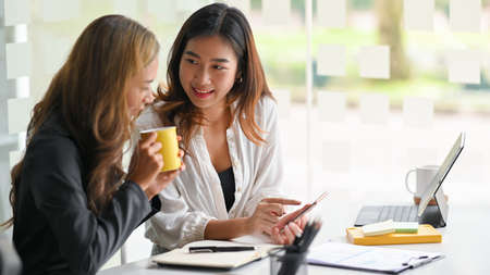 Happy cheerful employees chatting and talking about an interesting online content on smartphone.の写真素材
