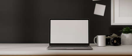 Simple modern workplace with laptop computer white display mockup on white worktable with decor over black wall. 3d rendering, 3d illustrationの写真素材