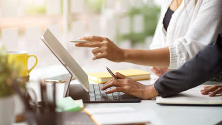 Cropped image with a side view of two businesswomen speaking in a meeting and working on a digital tablet computer. Corporate projectsの写真素材