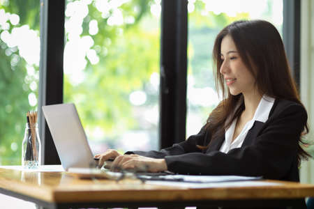 Charming young businesswoman working on laptop computer in modern working area. female assistant using notebook in office.の写真素材