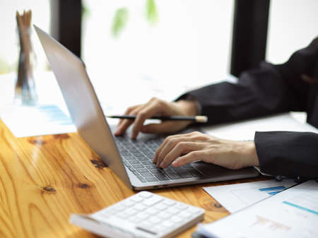 Cropped image of female accountant working on laptop computer with financial report paperworks at office.の写真素材