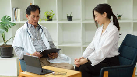 Middle-aged male therapist having a private medical examination with a female patient in his clinic office. medical people concept.の写真素材