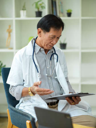 A middle-aged specialist male doctor checks and reads a treatment plan for a patient who has been injured on a medical clipboard.の写真素材