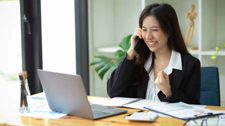 A happy young female employee received great news from her phone call. Getting promotions, new jobs, being successful.の写真素材