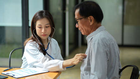 A young female doctor uses a stethoscope to check the pulse of an aged male patient. heart rate, heart beat.の写真素材