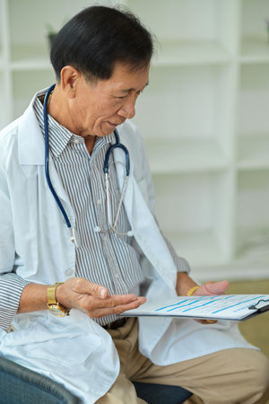Portrait of Successful specialist male physician reading a drug prescription on medical clipboard in his room.の写真素材