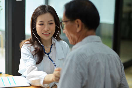 Young asian female doctor examining middle aged male patient in hospital office. Healthcare medical people concept.の写真素材
