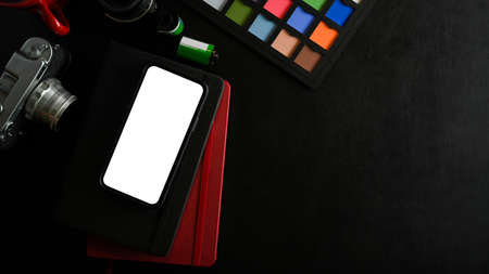 Copy space on black background with smartphone blank screen mockup, camera and colour checker board. top view, flat layの写真素材